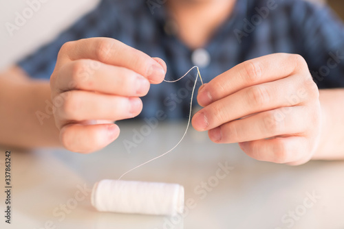 Threading a white thread into a needle. Making a homemade protective mask