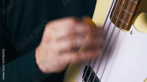 CU: funky bassist in black pullover plays white guitar with yellow pick in vertical position close view photo