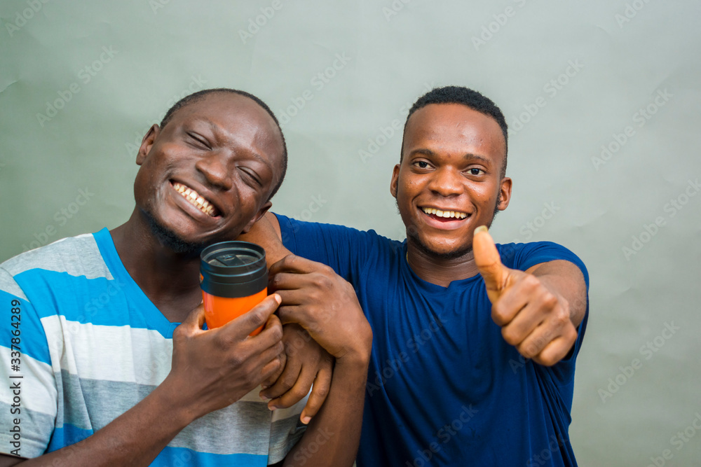two young handsome african men isolated over grey background feeling excited as they holds a coffee cup and did thumbs up two young handsome african men isolated over grey background feeling excited as they holds a coffee cup and did thumbs up