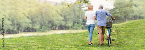 Elder healthy leisure lifestyle,Senior couple walking their bike along happily talking in the park, rear view of an older caucasian walk in a park, Banner image, Health care insurance