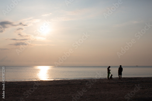 Happy family holidays. Joyful father, mother, baby son walk with fun along edge of sunset sea surf on black sand beach. Active parents and people outdoor activity on summer vacations with children. 