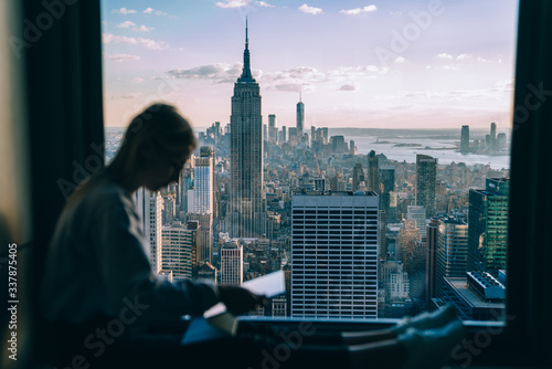 Selective focus on cityscape scenery from highrise panoramic window with millennial woman using modern technology on blurred frontage, above view from building on Manhattan district in New York © BullRun