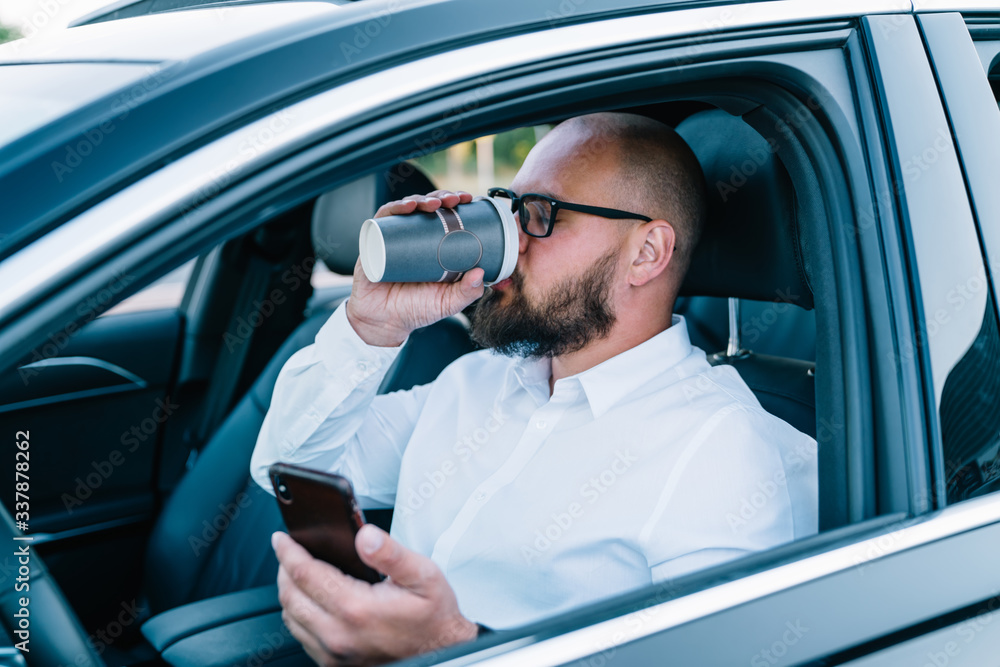 Confident male driver in optical spectacles for provide eyes protection concentrated on smartphone using while testing autopilot self-driving in advanced expensive automobile, transportation concept Confident male driver in optical spectacles for provide eyes protection concentrated on smartphone using while testing autopilot self-driving in advanced expensive automobile, transportation concept