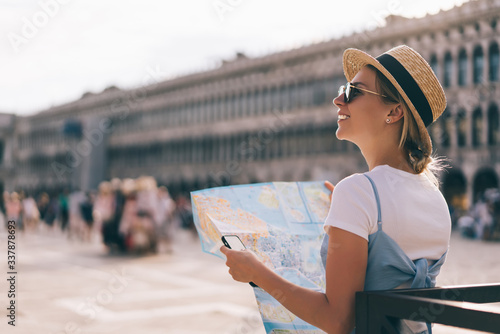 Caucasian female tourist in trendy apparel standing at popular Venezian San Marco Square, millennial woman with mobile technology and paper map visiting romantic city during solo journey to Italy photo