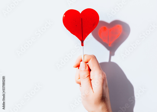 Female hand holds lollipops, red hearts candy with shadow. Love minimal concept. Valentine day. Top view.