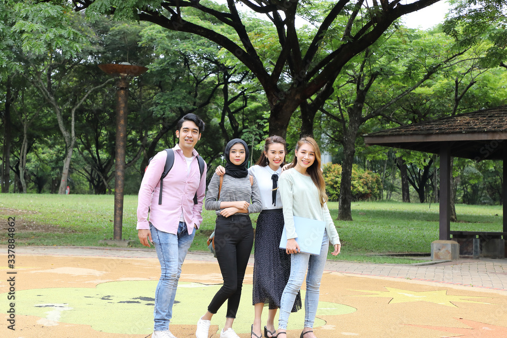 Fototapeta premium Young asian malay chinese man woman outdoor park walk stand study talk discuss point laptop file book backpack mingle fun happy