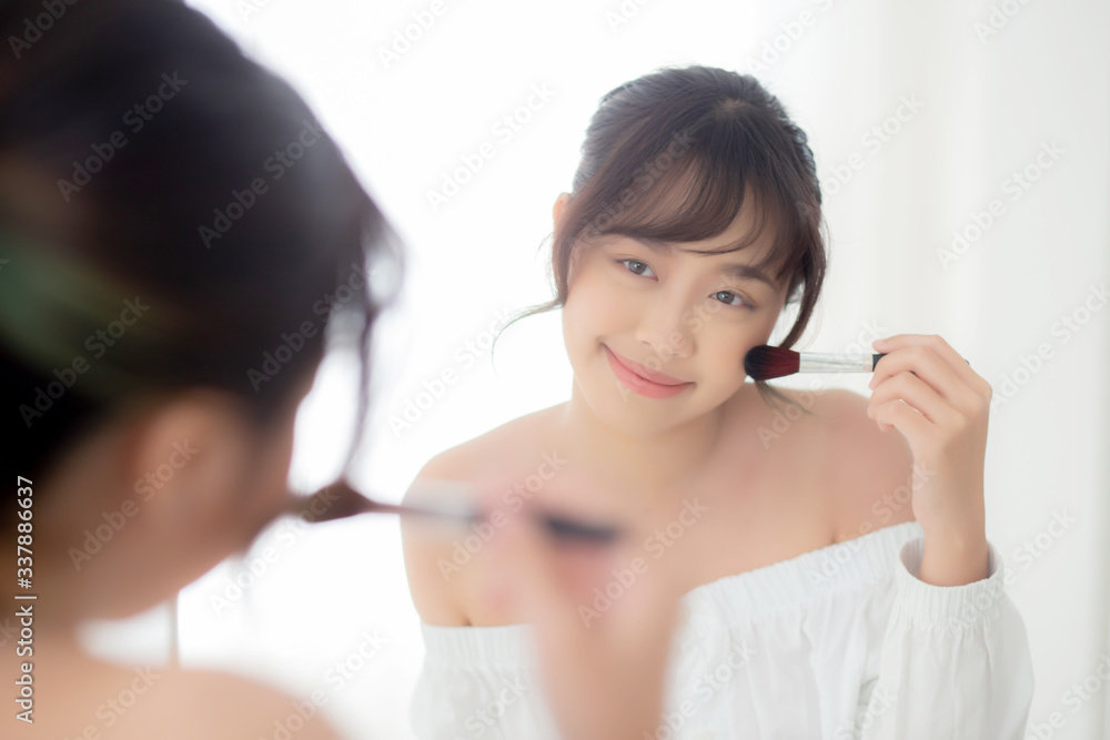 Beauty portrait young asian woman smile with face looking mirror applying makeup with brush cheek in the bedroom, beautiful of girl holding blusher, skin care and cosmetic concept. Beauty portrait young asian woman smile with face looking mirror applying makeup with brush cheek in the bedroom, beautiful of girl holding blusher, skin care and cosmetic concept.