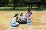 Young asian malay chinese man woman outdoor park sit on ground study talk discuss point laptop file book backpack mingle fun meet