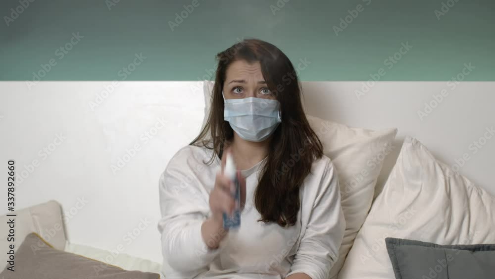 Worried cute female in self isolation scared of viruses and bacteria, looks depressed, paranoia during coronavirus outbreak. Girl in protective mask nervously spits antibacterial spray around herself Worried cute female in self isolation scared of viruses and bacteria, looks depressed, paranoia during coronavirus outbreak. Girl in protective mask nervously spits antibacterial spray around herself