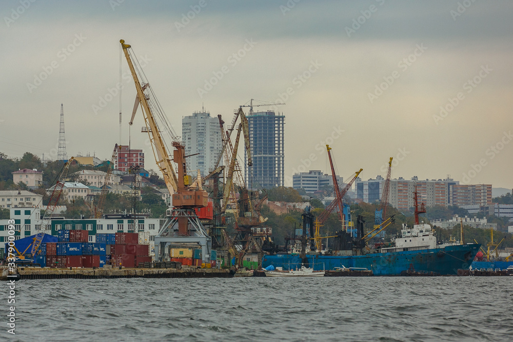 Vladivostok Industrial Marine Facade. Cargo cranes in the trading port of a large sea city. Commercial cargo ships stand in port against the background of tall cranes.