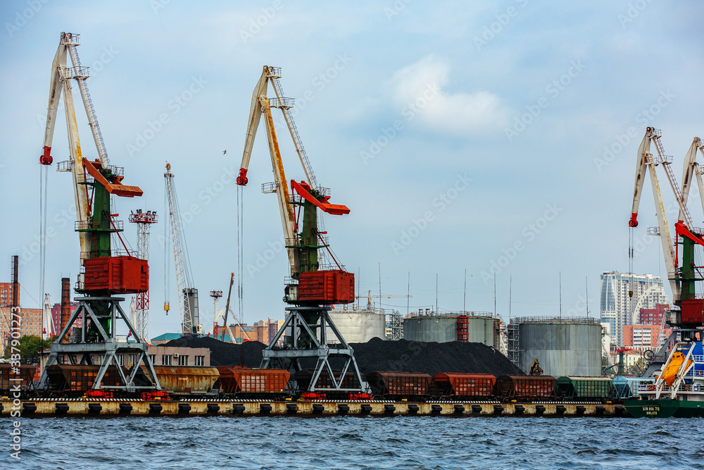Vladivostok Industrial Marine Facade. Cargo cranes in the trading port of a large sea city. Commercial cargo ships stand in port against the background of tall cranes. Vladivostok Industrial Marine Facade. Cargo cranes in the trading port of a large sea city. Commercial cargo ships stand in port against the background of tall cranes.