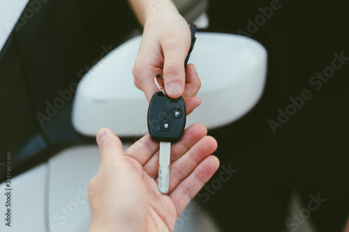 A male dealer hand giving car keys to female person, close-up photo outdoor with car in background