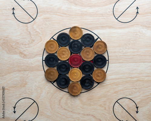 Carrom men and red arranged on the board around the center star.
