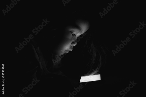 A young Asian woman is sleeping, watching mobile phones in the dark.