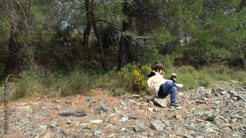 Fethiye, Turkey - 27d of March 2020: 4K Child shakes out his shoes sitting on a stone in the forest
 photo