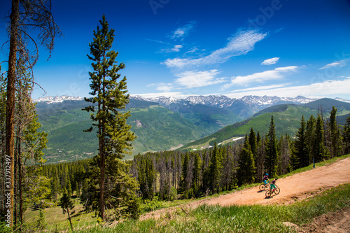 Fotografie A pair of mountain bikers ride up a dirt path on a sunny summer day in Vail, Colorado