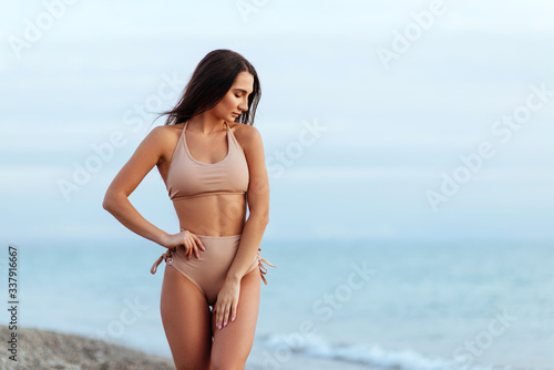 Portrait of attractive young woman in bikini on the beach. Young caucasian female model posing in swimsuit on the sea shore and smiling.