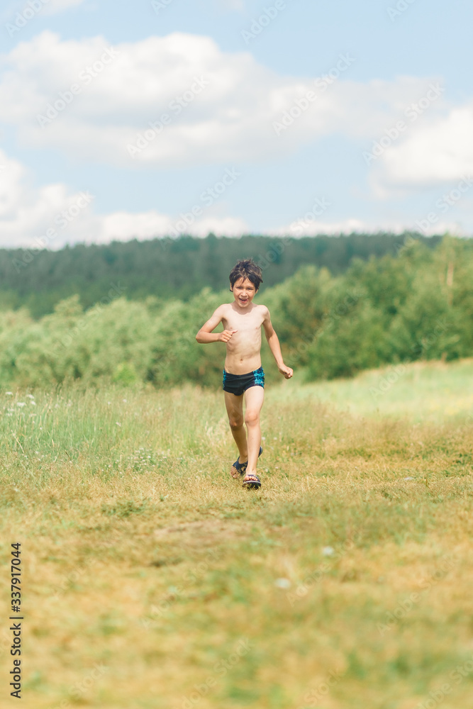 a boy in blue swimming trunks runs on a field of grass in the summer under the hot sun
