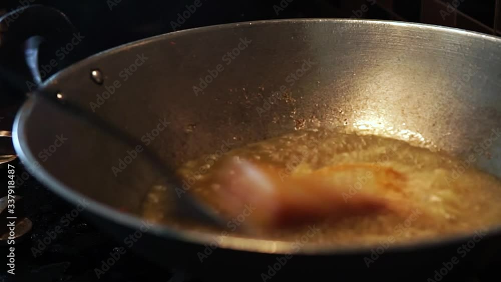 Close up view of houswife putting and frying a Tilapia fish in a boiling oil in a metal wok at the kitchen. Zooming out footage. Close up view of houswife putting and frying a Tilapia fish in a boiling oil in a metal wok at the kitchen. Zooming out footage.