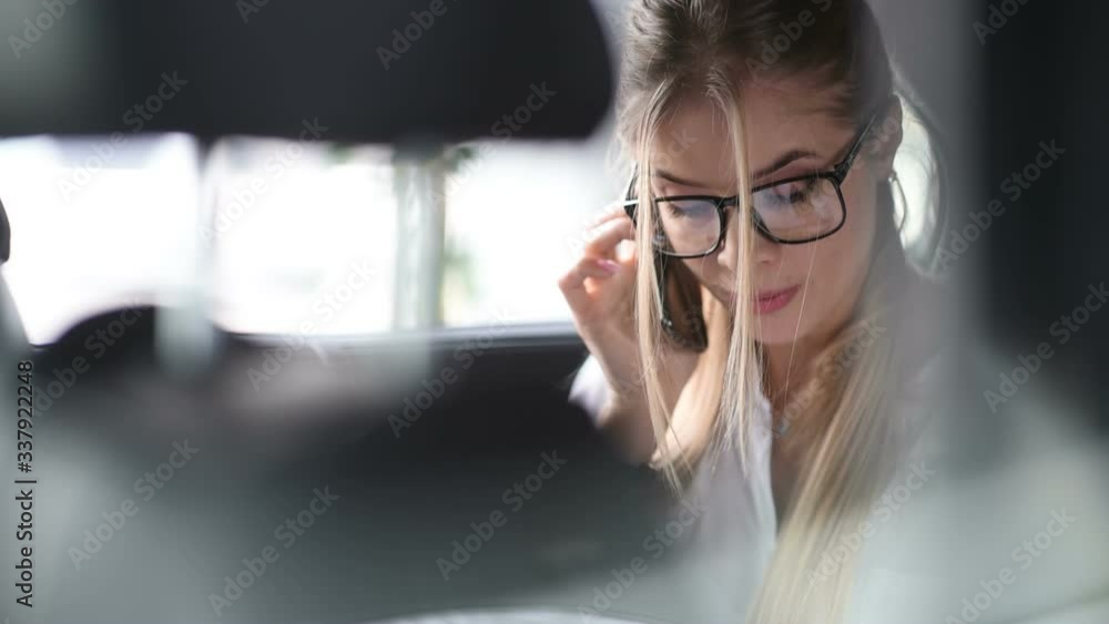 Beautiful business woman is talking on the mobile phone and using a tablet with papers while sitting on back seat in the car. Beautiful business woman is talking on the mobile phone and using a tablet with papers while sitting on back seat in the car.