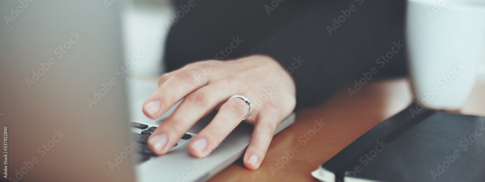 Close-up of woman working on computer. Book and cup on the table. Soft focus image