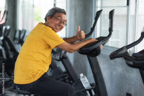 Old happy man cycling on gym machine