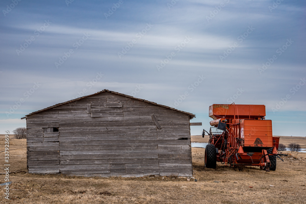 Vintage red combine abandoned beside an old barn in a prairie farmyard in Saskatchewan, Canada