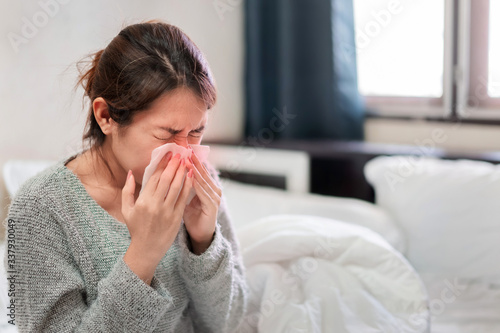 Sick asian woman have hight fever flu and sneezing into tissue on bed in bedroom, Healthcare and prevent the spread infection corona virus concept, Selective focus.