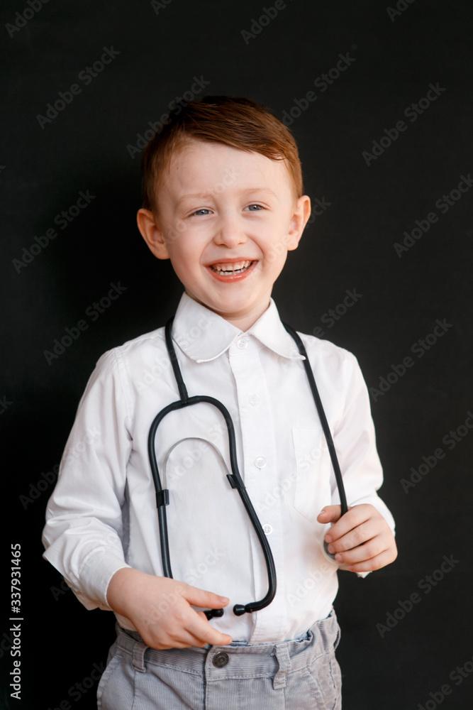 Smiling little boy in medical uniform playing with stethoscope Black background. Smiling little boy in medical uniform playing with stethoscope Black background.