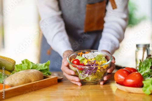 Closeup image of a female chef cooking and holding a bowl of fresh mixed vegetables salad in kitchen