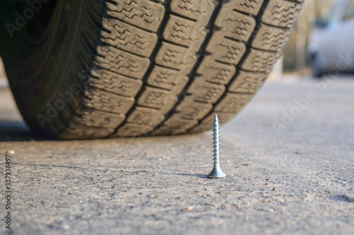 Bild auf Leinwand A self-tapping screw stands on the road in an upright position in front of the car wheel