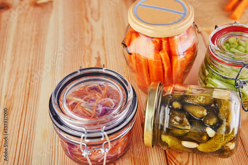 Fermented preserved vegetarian food concept. Sour sauerkraut, pickled carrots, pickles, pickled celery glass jars on a wooden kitchen table. The concept of canned food.