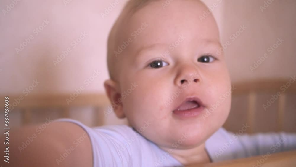 Cute Baby Close-up. Child Looks At Camera And Reaches Hand. Nine Month Baby Boy In A Crib In The Nursery Cute Baby Close-up. Child Looks At Camera And Reaches Hand. Nine Month Baby Boy In A Crib In The Nursery