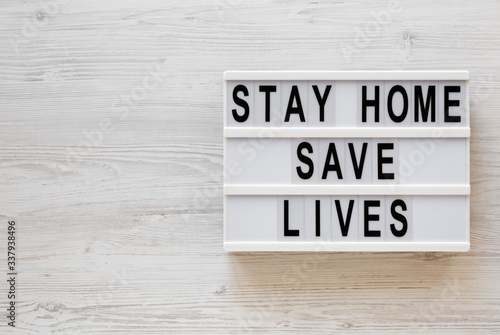 'Stay Home Save Lives' words on a lightbox on a white wooden background, top view. Overhead, from above, flat lay. Space for text.