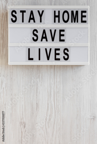 'Stay Home Save Lives' words on a lightbox on a white wooden surface, top view. Overhead, from above, flat lay.
