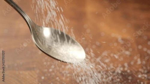 Stack of footage: White sugar fall through teaspoon down on a brown wood background. Slow motion. HD