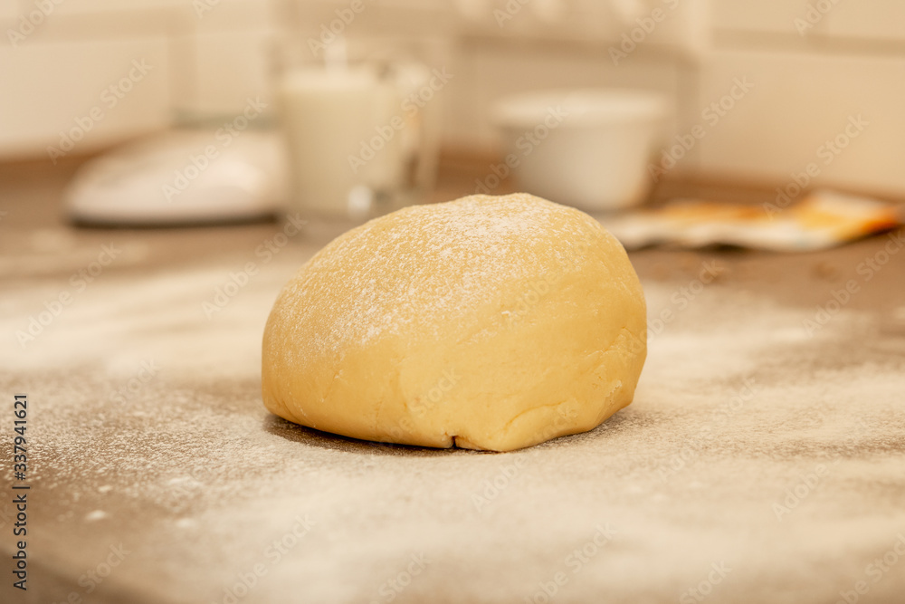 closeup raw round dough lies on a kitchen table in white flour and is ready for the baking process. Blurred background with interior objects and utensils closeup raw round dough lies on a kitchen table in white flour and is ready for the baking process. Blurred background with interior objects and utensils