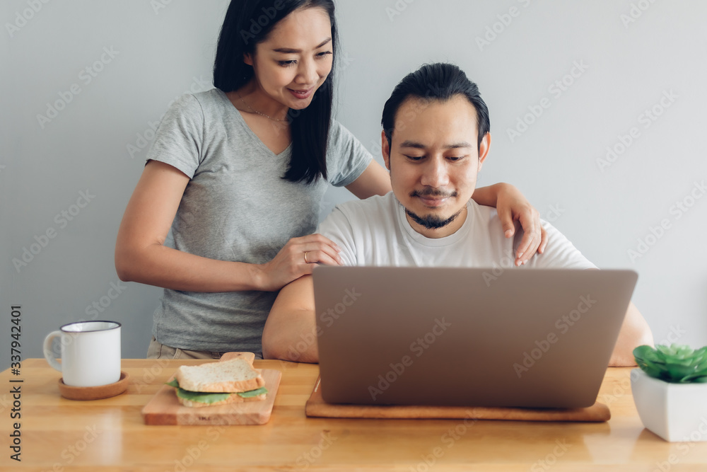 Happy Asian man is working online with his wife support in concept of work from home. Happy Asian man is working online with his wife support in concept of work from home.