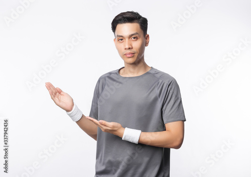 Young asian man in sport outfits pointing to copyspace and looking to camera isolated on white background.