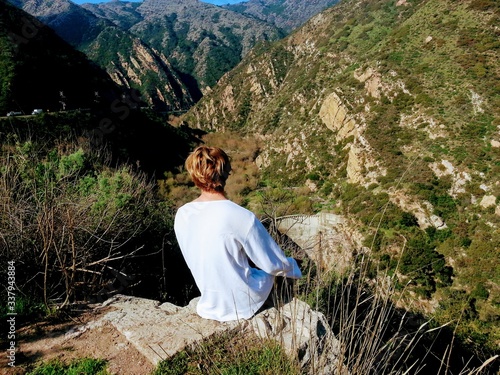 Single young man sitting on a rock precipice enjoying the outdoor scenic beauty over looking Malibu Canyon and mountains, a popular tourist place to visit and hike because of its beautiful scenery