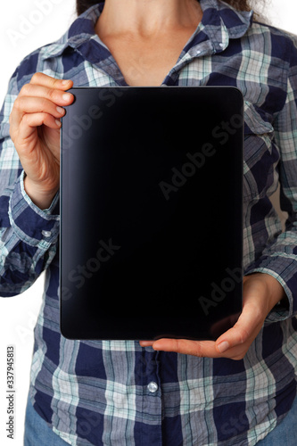 Young woman in checked shirt holding empty black electronic tablet with copy space
