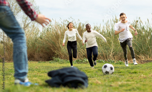 multi nationalities teenagers play football through green lawn in summer in park