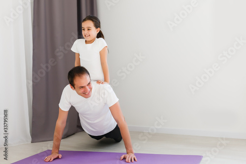 Handsome young father and his cute little daughter are doing reverce plank with leg raise on the floor at home. Family fitness workout.