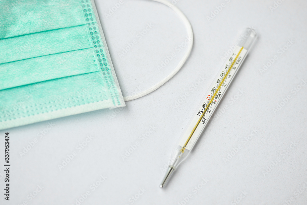 a mercury thermometer and a green face mask on white background a mercury thermometer and a green face mask on white background