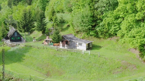 Aerial: zooming in shot on two lonely cabbins within a forest during summer day. photo