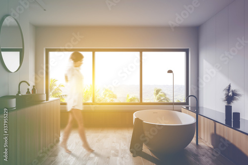 Woman walking in white sunlit bathroom