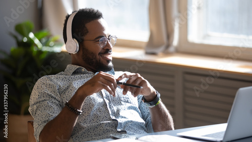 Distracted from job study happy millennial african american man in glasses listening to favorite audio music, looking away, thinking of future, enjoying pause break time alone at workplace home.