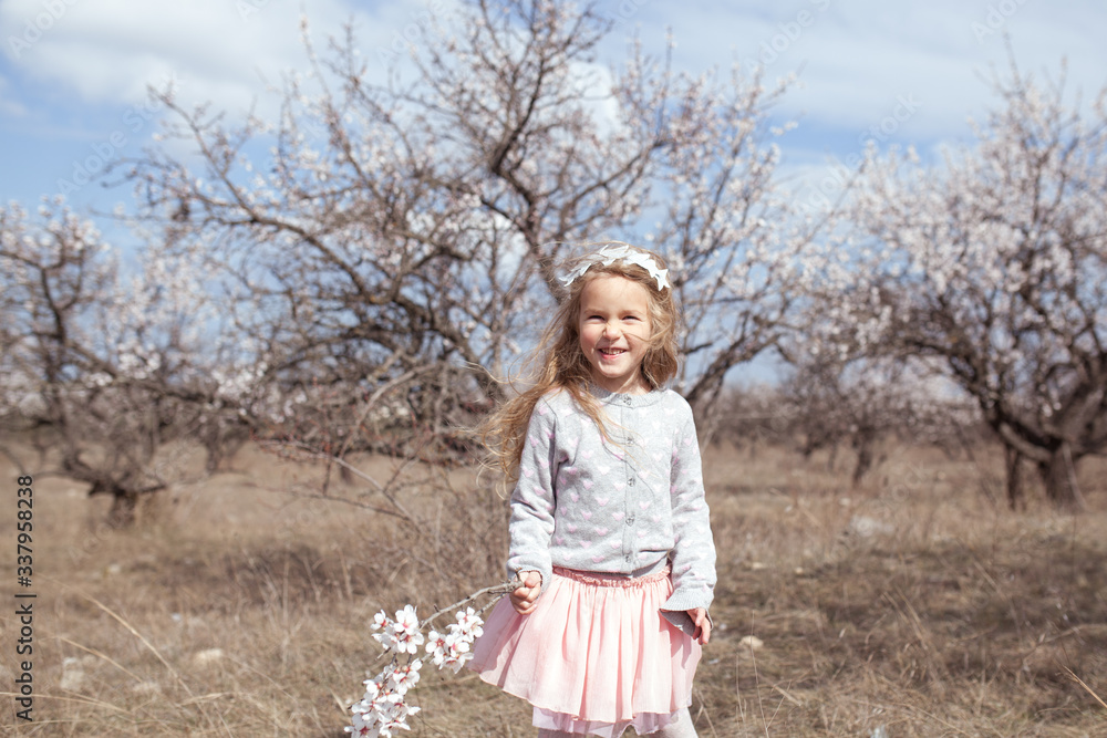 portrait of a pretty happy girl on a background of almond trees in bloom, the child is laughing portrait of a pretty happy girl on a background of almond trees in bloom, the child is laughing