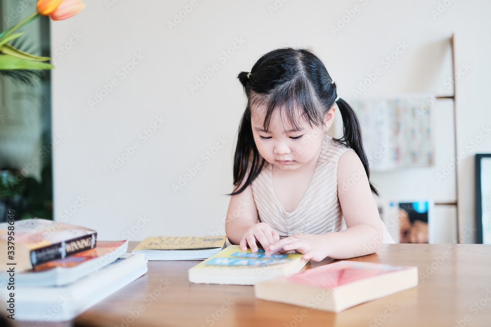 Cute asian girl learning by reading and studying books and playing at home in the living room sitting, home schooling education for children, feeling happy cheerful, and enjoying staying at home Cute asian girl learning by reading and studying books and playing at home in the living room sitting, home schooling education for children, feeling happy cheerful, and enjoying staying at home