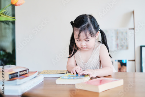 Cute asian girl learning by reading and studying books and playing at home in the living room sitting, home schooling education for children, feeling happy cheerful, and enjoying staying at home